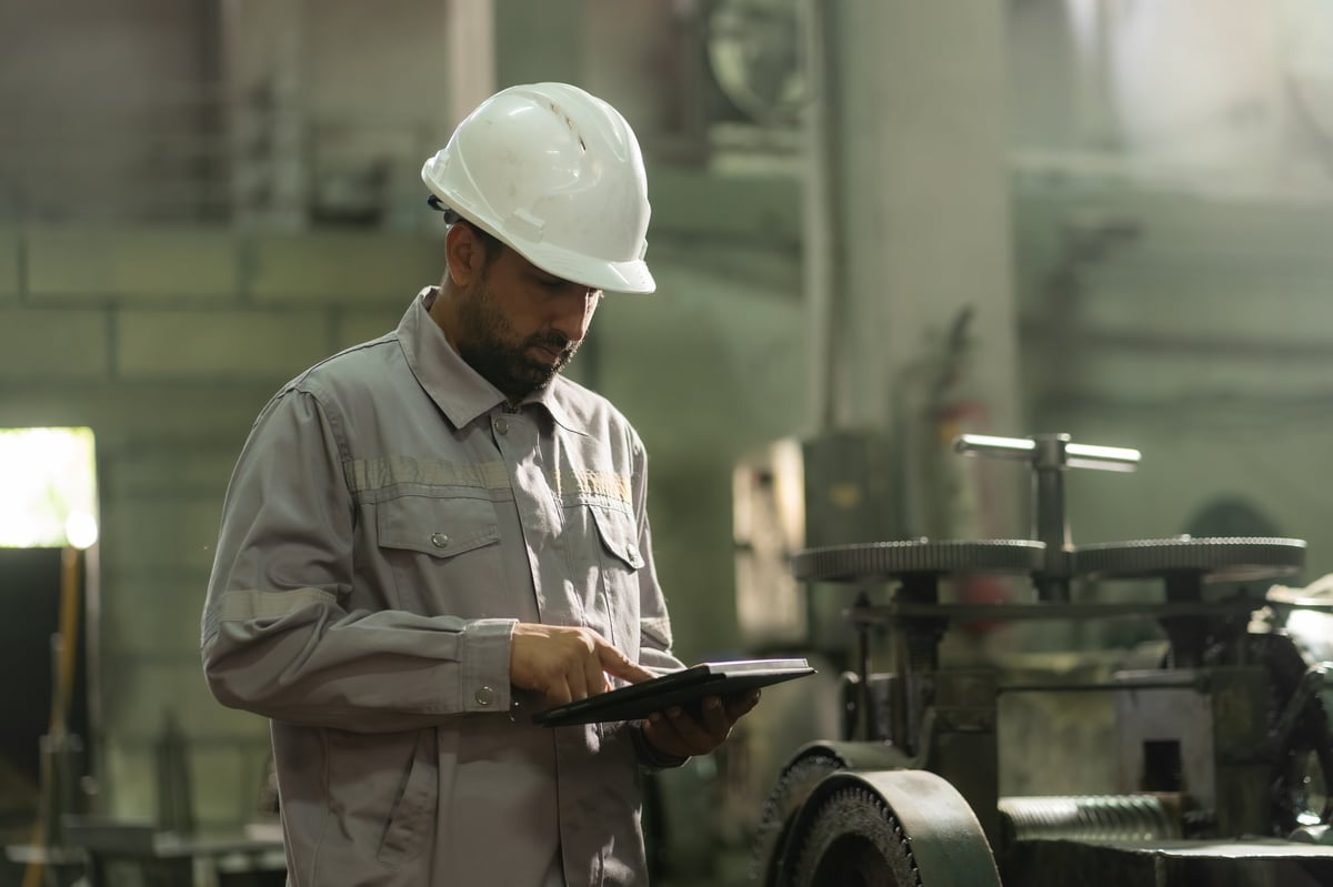 Engineer using a digital tablet to assess heavy machinery in an industrial factory